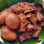 Plate with braised meat and three hard-boiled eggs on a banana leaf liner.