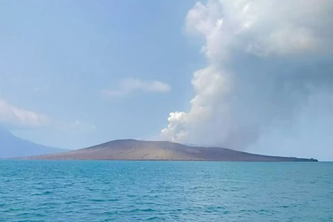 Calm blue sea with a flat volcanic island in the distance and white smoke rising from a crater.