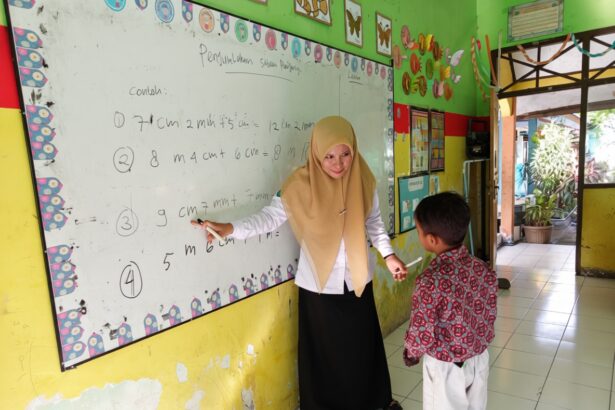 Teacher in a beige hijab explains math problems on a whiteboard to a young student in a colorful classroom.