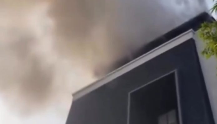 Modern dark building with thick smoke billowing from the roof, suggesting a fire in progress.
