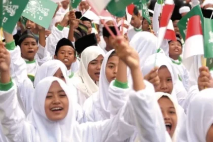 Group of smiling girls in white hijabs waving green and white flags at a rally.