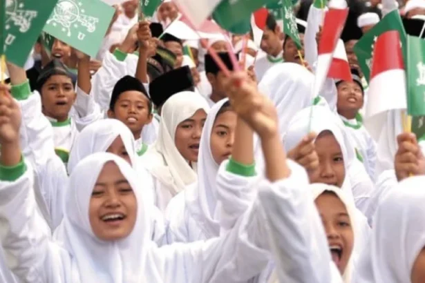 Group of smiling girls in white hijabs waving green and white flags at a rally.