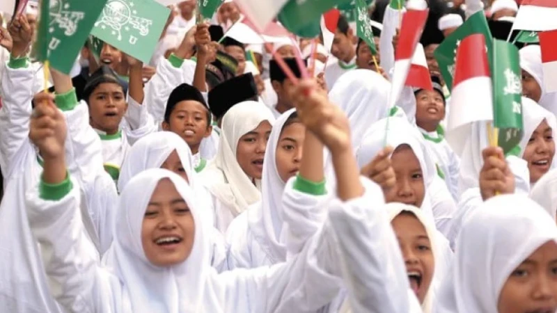 Group of smiling girls in white hijabs waving green and white flags at a rally.