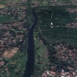 Aerial view of a winding river dividing a town on the left from farmland on the right, with a north arrow overlay.