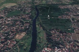 Aerial view of a winding river dividing a town on the left from farmland on the right, with a north arrow overlay.