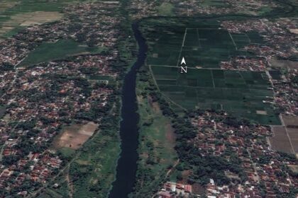 Aerial view of a winding river dividing a town on the left from farmland on the right, with a north arrow overlay.