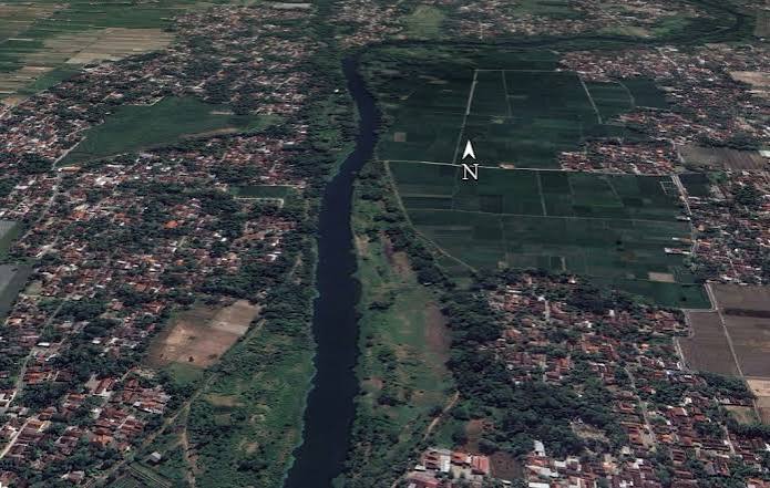 Aerial view of a winding river dividing a town on the left from farmland on the right, with a north arrow overlay.
