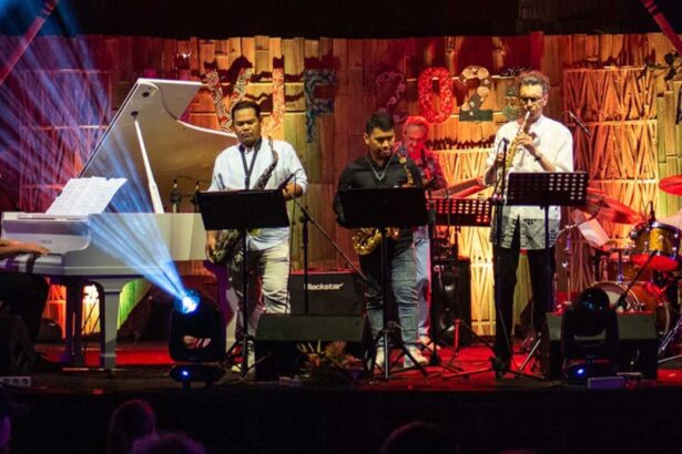 Live band performing on stage: pianist at left, saxophonists in center, trumpet player at right, with colorful stage lighting.