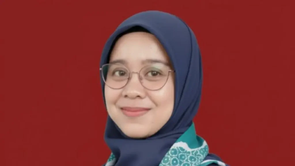 Smiling woman wearing a navy blue hijab and round glasses against a red backdrop.