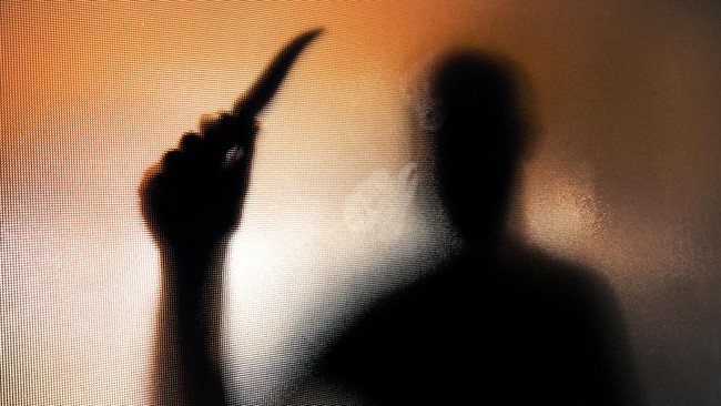 Blurred silhouette of a person with a raised knife against an orange-tinted background.