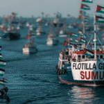 A flotilla of boats at sea with Palestinian flags; the lead boat's banner reads 'FLOTILLA GLOBAL SUMUD'.