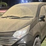 Dusty dark SUV parked on grass at night, with mud splatters coating the body and windshield wipers resting on the windshield