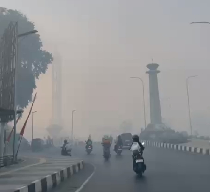 A hazy urban street scene with several motor scooters riding toward the camera and a few pedestrians on the sidewalk; a tall column-like monument is visible in the distance.