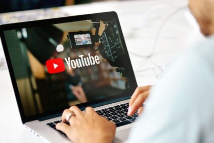 Person typing on a laptop displaying the YouTube logo and a video camera, suggesting video creation or uploading to YouTube