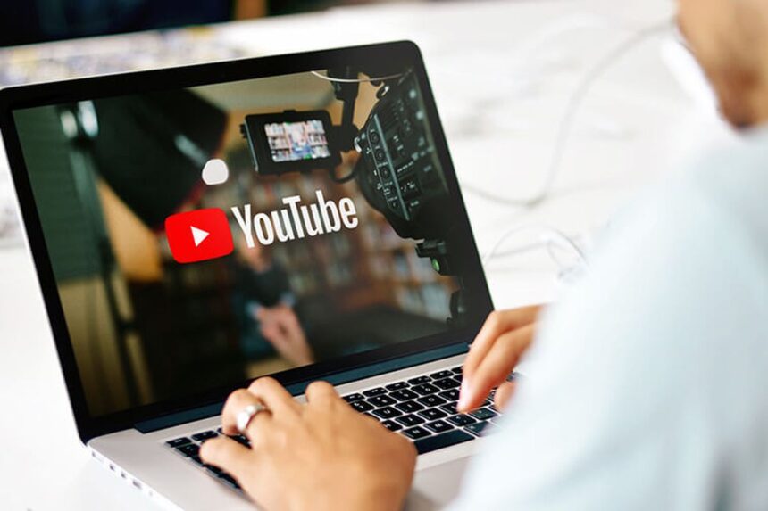 Person typing on a laptop displaying the YouTube logo and a video camera, suggesting video creation or uploading to YouTube