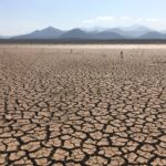 Dry, cracked earth of a parched lakebed with distant mountains on the horizon under a clear sky.