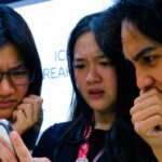 Three young people gathered around a smartphone, frowning and looking concerned.