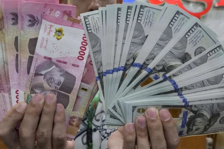 Hands hold a fan of cash: pink Thai baht notes on the left and fanned US $100 bills on the right.