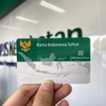 Indonesian health card Kartu Indonesia Sehat (BPJS Kesehatan) held up in front of a blurred backdrop