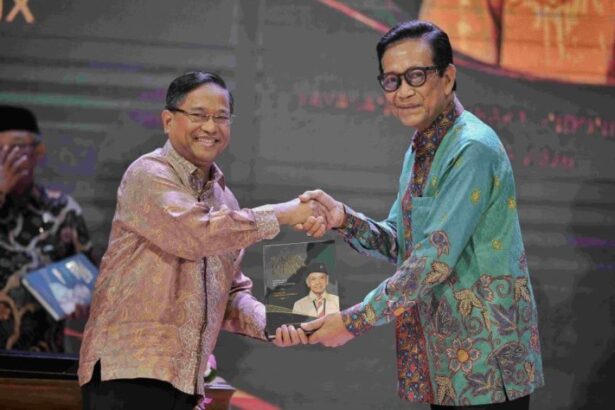 Two men on a stage shake hands while one presents a plaque featuring a portrait, during a formal event.
