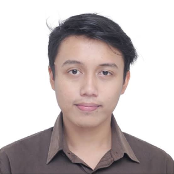 Portrait of a young man with short black hair in a brown collared shirt, neutral expression, white background.