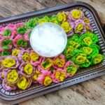 Colorful flower-shaped dumplings in pink, purple, yellow, and green arranged on a brown tray with a bowl of ice in the center.