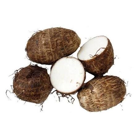 Five taro roots on a white background, one cut in half to reveal white starchy flesh in the center.