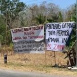 Two handwritten protest banners beside a road, criticizing local officials' integrity and permit handling, in a dry rural area.