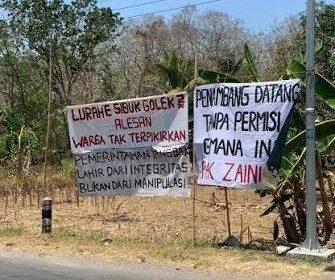 Two handwritten protest banners beside a road, criticizing local officials' integrity and permit handling, in a dry rural area.