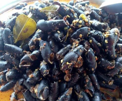 Dark squid ink pasta with garlic bits and herbs served on an orange plate, a dish with a glossy sauce and bay leaf in the mix.