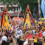 Crowd at a colorful festival featuring two large dragon costumes dancing among onlookers, with banners and participants taking photos.