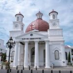 White church with a red dome, two clock towers, and a columned portico under a blue sky.