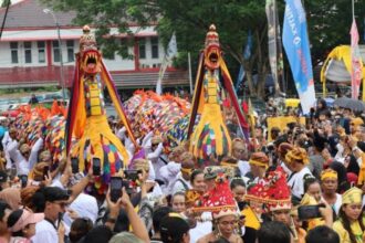 Crowd at a colorful festival featuring two large dragon costumes dancing among onlookers, with banners and participants taking photos.