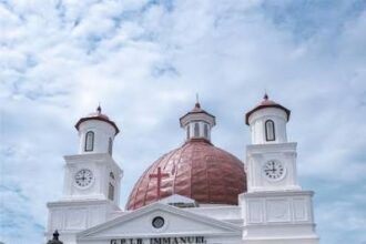 White church with a red dome, two clock towers, and a columned portico under a blue sky.