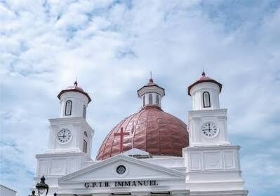 White church with a red dome, two clock towers, and a columned portico under a blue sky.