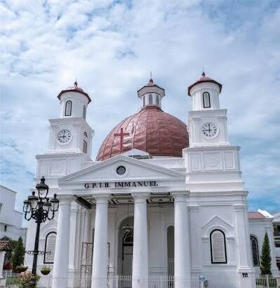 White church with a red dome, two clock towers, and a columned portico under a blue sky.