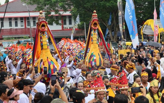 Crowd at a colorful festival featuring two large dragon costumes dancing among onlookers, with banners and participants taking photos.