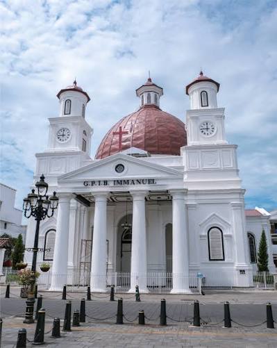 White church with a red dome, two clock towers, and a columned portico under a blue sky.
