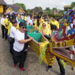 People in yellow outfits carry a colorful dragon boat with an ornate dragon head during a festival outside.