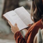 Person reading an open Bible outdoors, page showing 'Proverbs'.