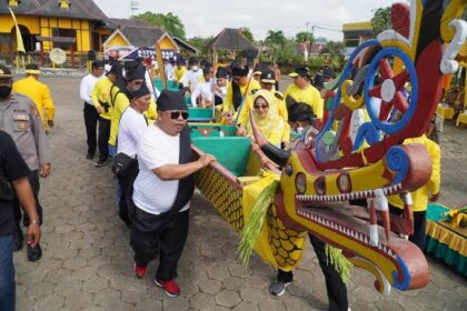 People in yellow outfits carry a colorful dragon boat with an ornate dragon head during a festival outside.