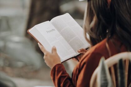 Person reading an open Bible outdoors, page showing 'Proverbs'.