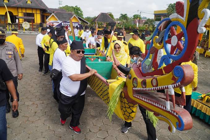 People in yellow outfits carry a colorful dragon boat with an ornate dragon head during a festival outside.