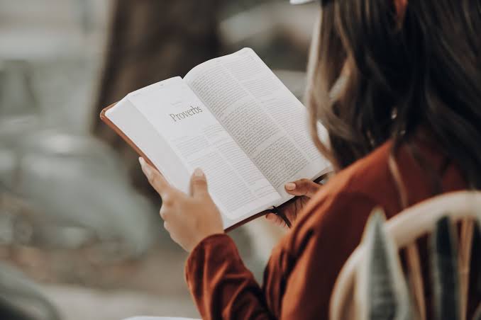 Person reading an open Bible outdoors, page showing 'Proverbs'.