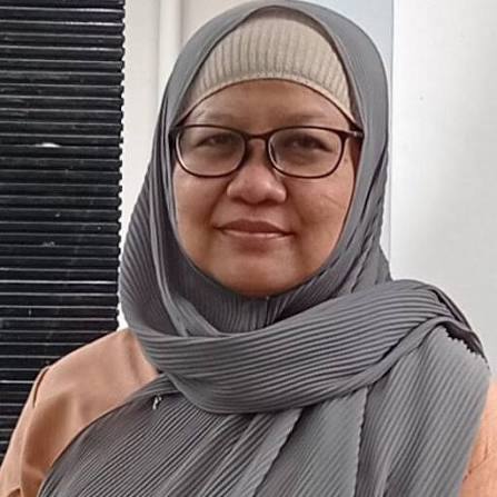 images 2 - Mabur.co Portrait of a woman wearing a gray hijab and black-rimmed glasses, looking at the camera with a slight smile.
