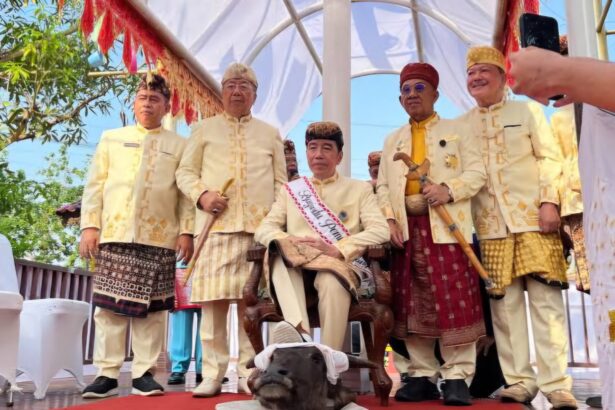 Group of men in cream traditional outfits standing on a decorated stage, with a small dog at their feet in front.