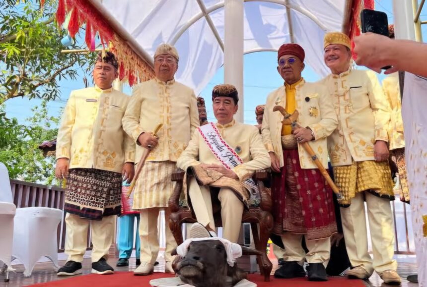 Group of men in cream traditional outfits standing on a decorated stage, with a small dog at their feet in front.