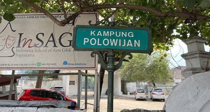 Green street sign reading 'KAMPUNG POLOWIJIAN' on a decorative post, with a banner and parked cars behind.