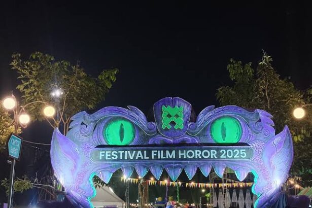 Nighttime festival entrance shaped like a purple monster with glowing green eyes; banner reads Festival Film Horor 2025, with a crowd underneath.