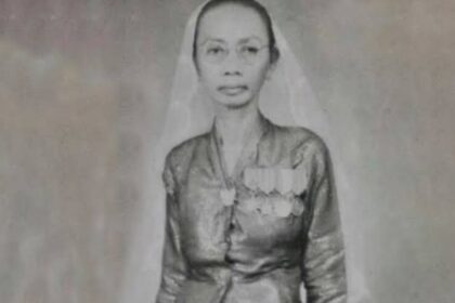 Black-and-white portrait of a woman wearing a veil and a medal-decorated dress, facing the camera.